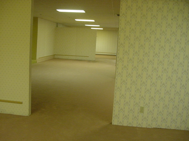 Photo of an empty room with dividing walls and yellow wallpaper giving it a liminal feel